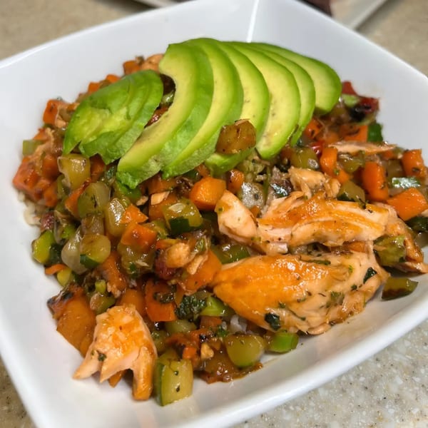 A white bowl filled with salmon, diced vegetables, and sliced avocado.