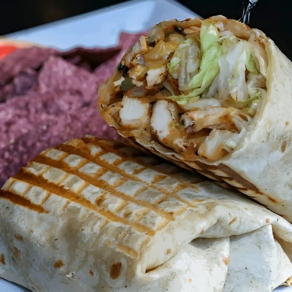 Two grilled chicken wraps, one open to show chicken and lettuce, on a white plate with purple food.