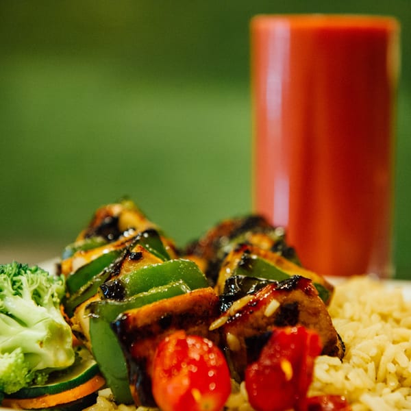 Grilled chicken and green pepper skewers with cherry tomatoes, rice, and broccoli, with a red drink.