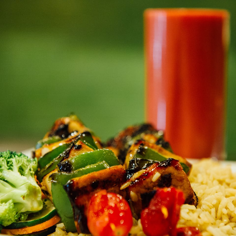 Grilled chicken and green pepper skewers with cherry tomatoes, rice, and broccoli, with a red drink.