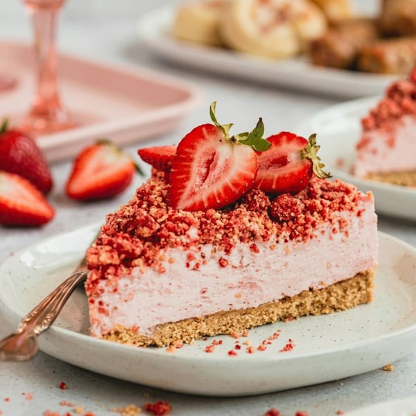 A slice of strawberry cheesecake with a graham cracker crust, topped with fresh strawberries and crumble.