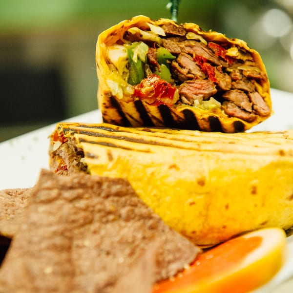 Grilled steak and vegetable wrap, cut in half, served with tortilla chips and a grapefruit slice.