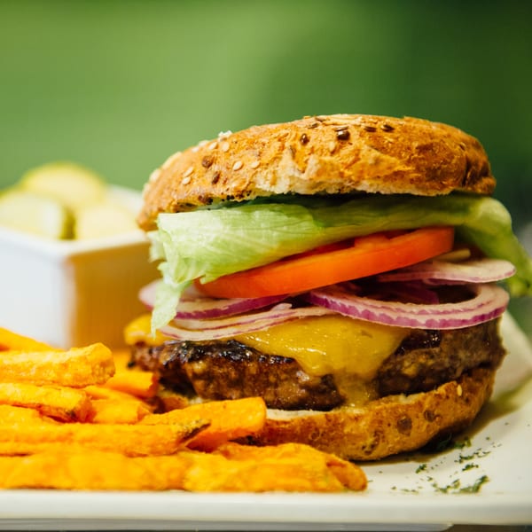 A juicy cheeseburger with lettuce, tomato, and red onion, served with sweet potato fries.