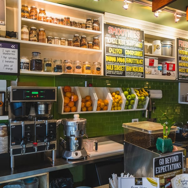 A smoothie bar with shelves of ingredients, fruit bins, blenders, and a menu board.