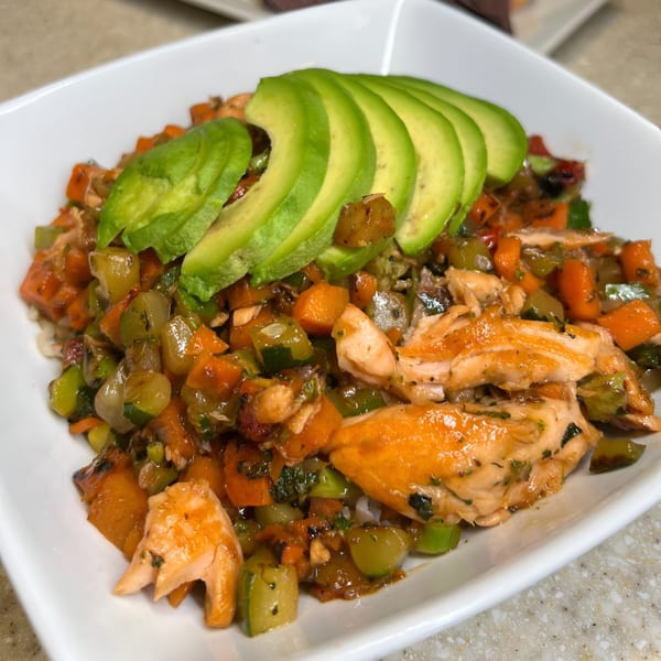 Salmon and diced vegetables, including carrots and zucchini, topped with sliced avocado in a white bowl.