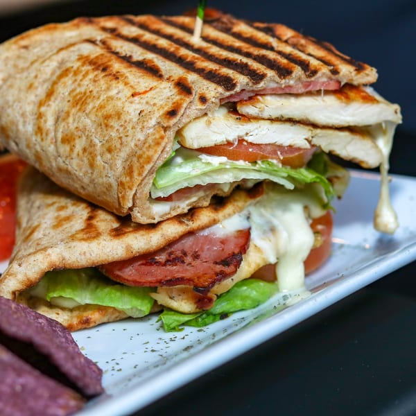 Grilled chicken and bacon panini with melted cheese, lettuce, and tomato, served with purple chips.