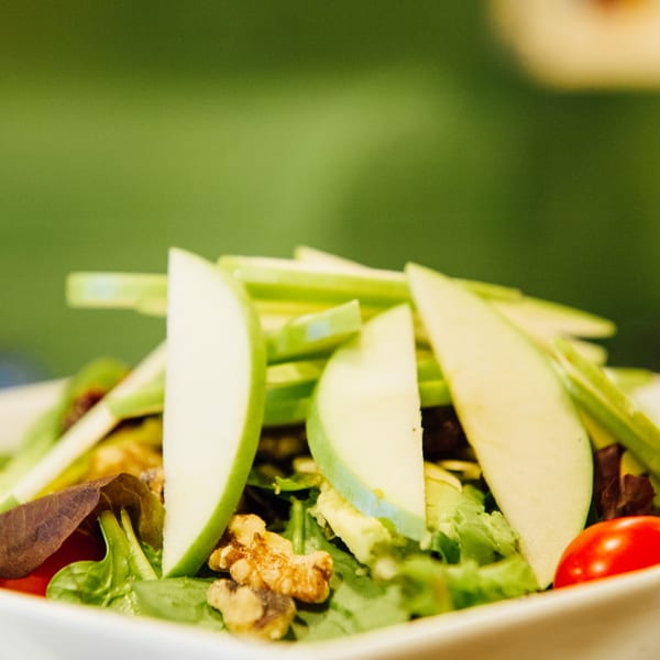 Close-up of a fresh salad with green apple slices, walnuts, and cherry tomatoes.
