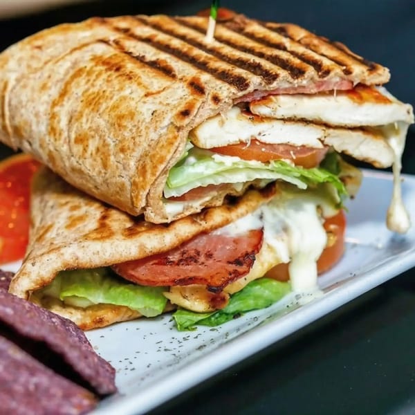 Grilled chicken and bacon panini with melted cheese, lettuce, and tomato, served with purple chips.