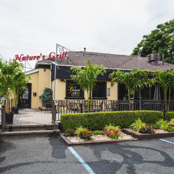 Exterior of Nature's Grill Cafe with outdoor seating, palm trees, and a landscaped garden.