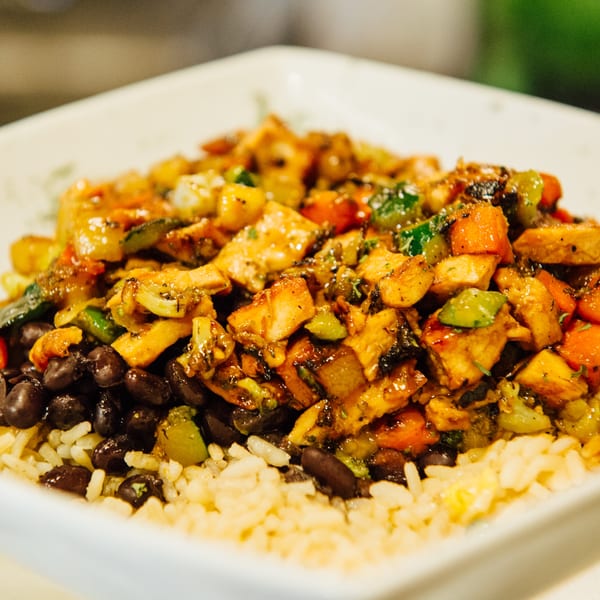 Close-up of a bowl with rice, black beans, and chicken with mixed vegetables.