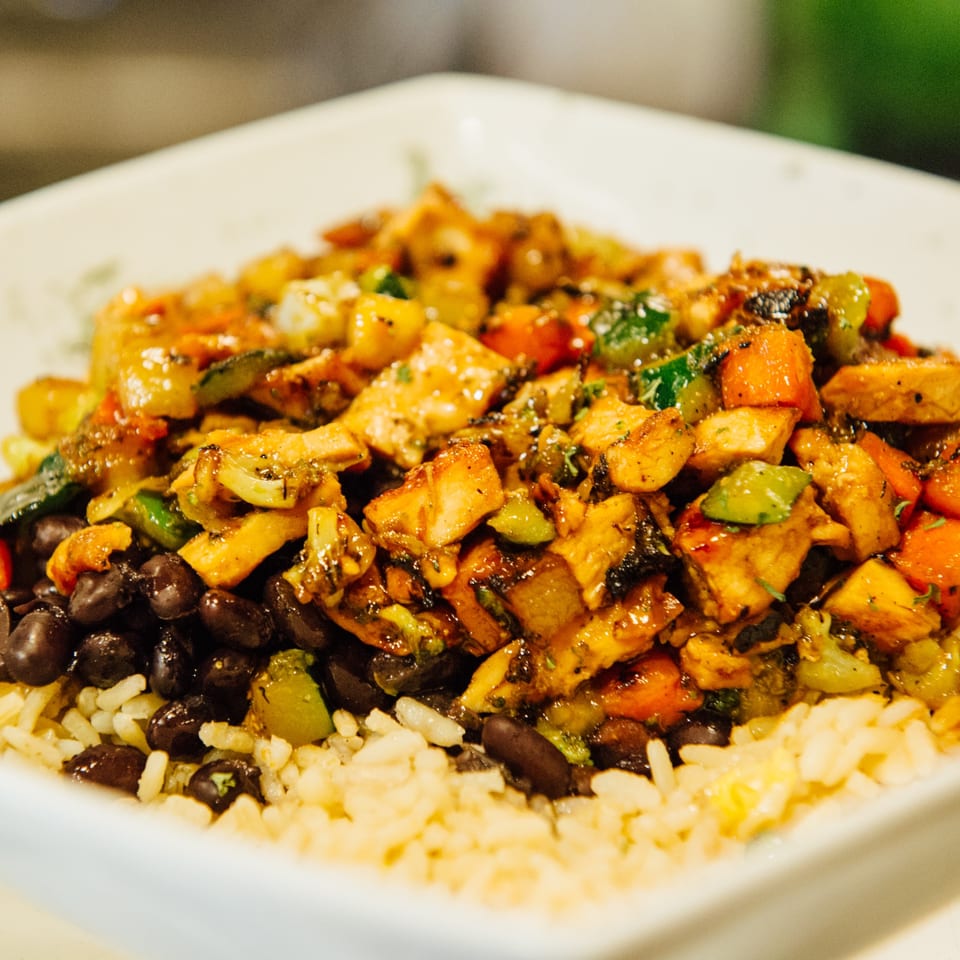 Close-up of a bowl with rice, black beans, and chicken with mixed vegetables.