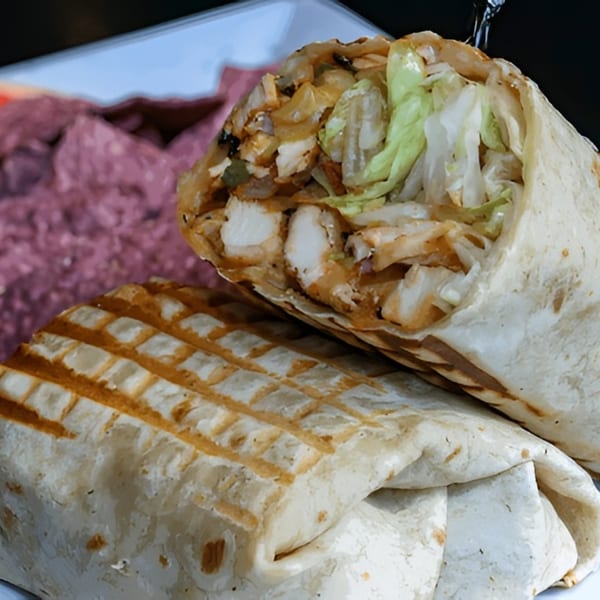 Two grilled chicken wraps with lettuce and sauce, one cut open, on a white plate with a purple side.