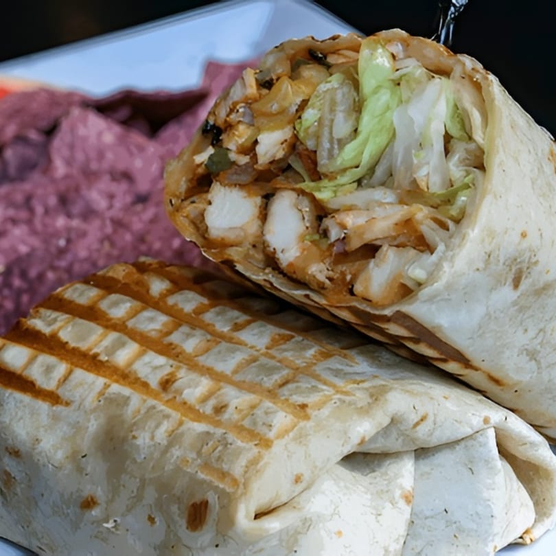 Two grilled chicken wraps with lettuce and sauce, one cut open, on a white plate with a purple side.