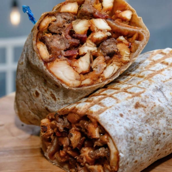 Two halves of a large burrito filled with chicken, bacon, and potatoes, on a wooden board.