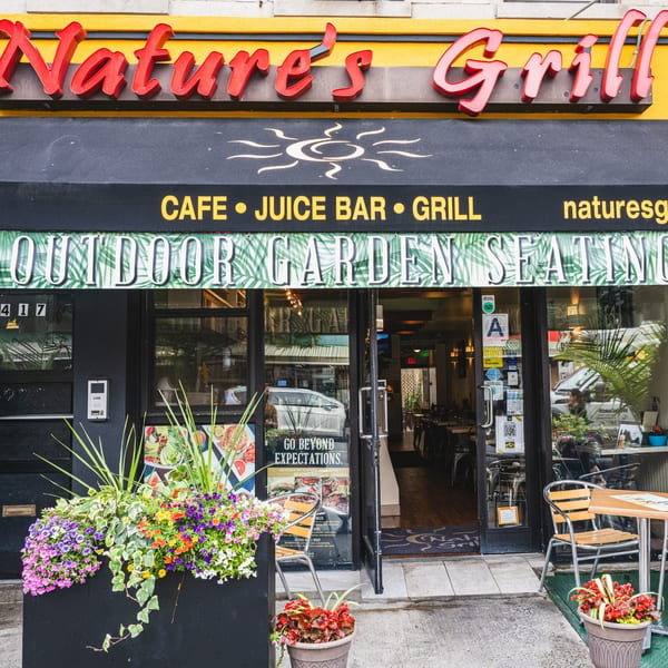 The storefront of Nature's Grill, featuring a black awning, outdoor seating, and colorful flower boxes.