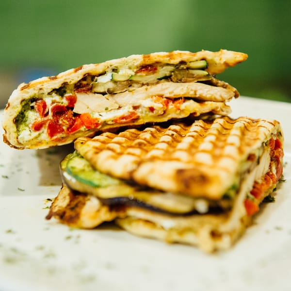 Two halves of a grilled panini sandwich filled with chicken, pesto, cheese, red peppers, and zucchini.