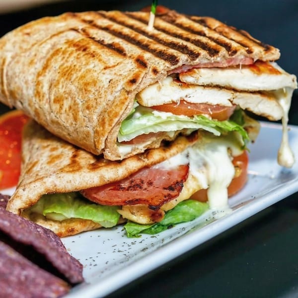Grilled chicken and bacon panini with melted cheese, lettuce, and tomato, served with purple chips.