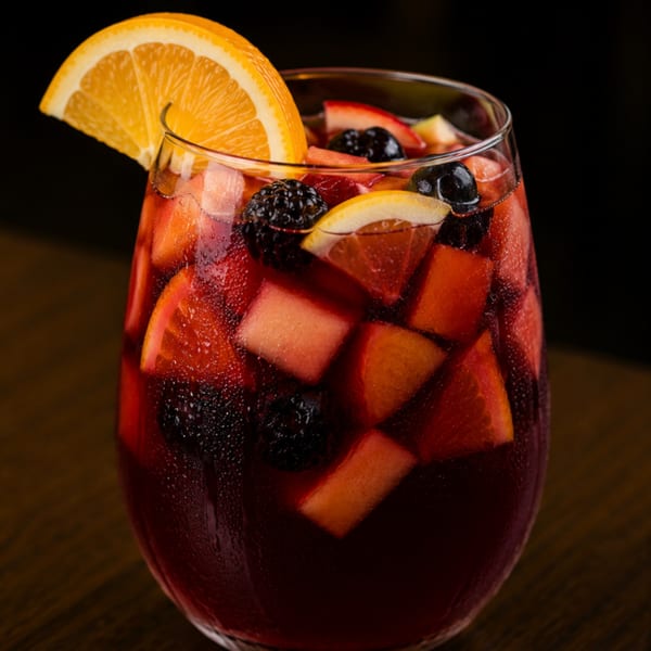 Close-up of a glass of red sangria with orange, lemon, strawberries, and blackberries.