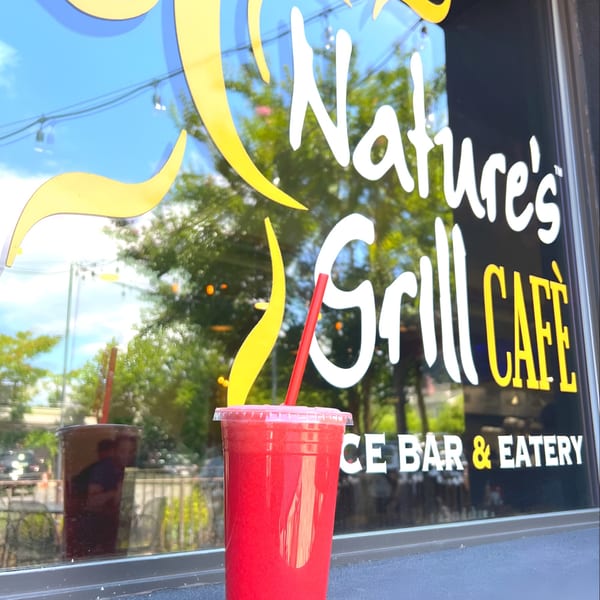 A vibrant red smoothie with a straw sits in front of Nature's Grill Cafe window.