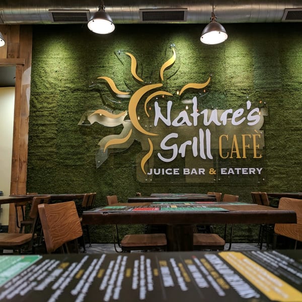 Nature's Grill Cafe logo on a moss wall, with tables and chairs in the foreground.